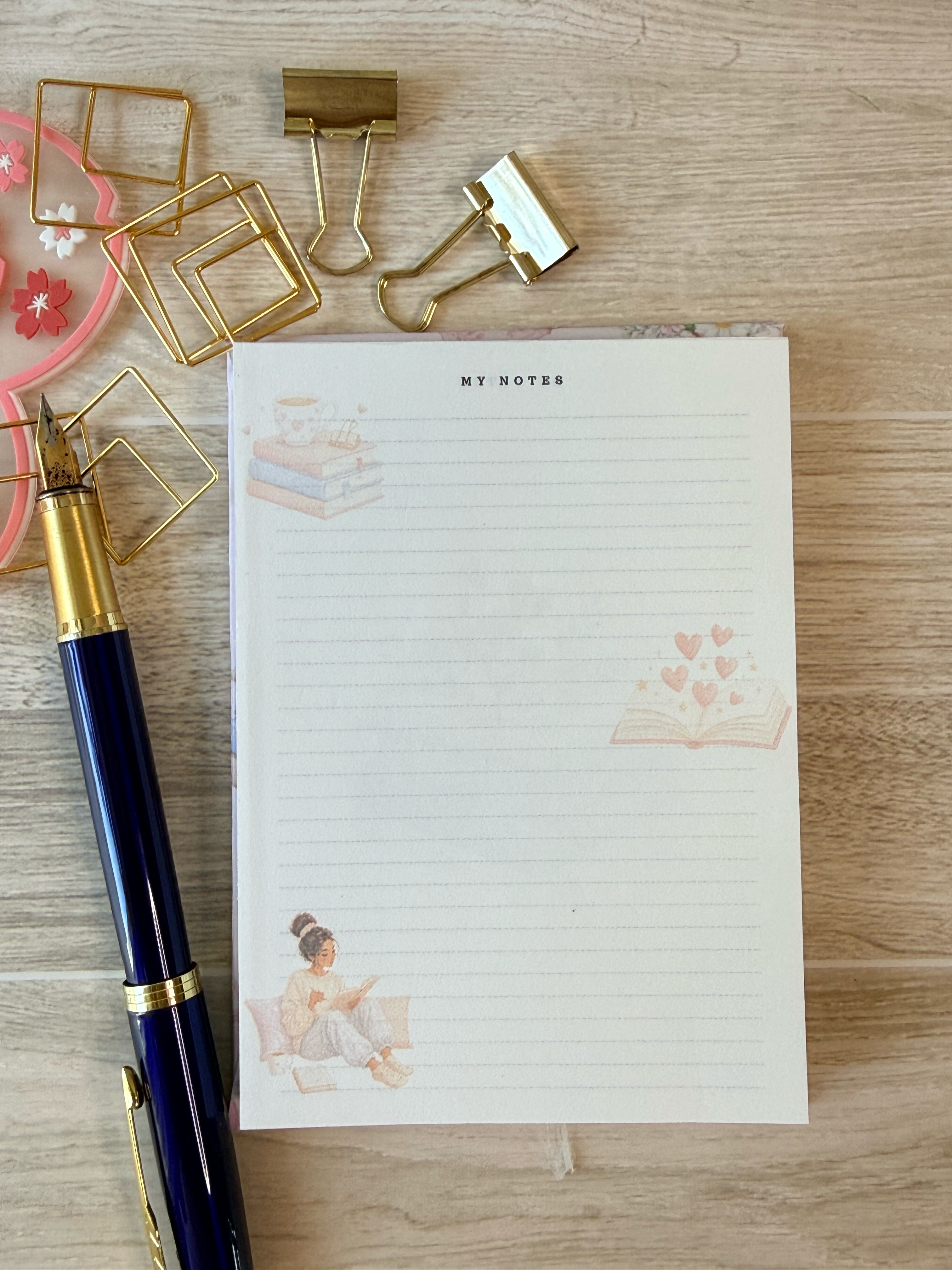 Notebook with decorative pages, gold paper clips, and a pen on a wooden surface