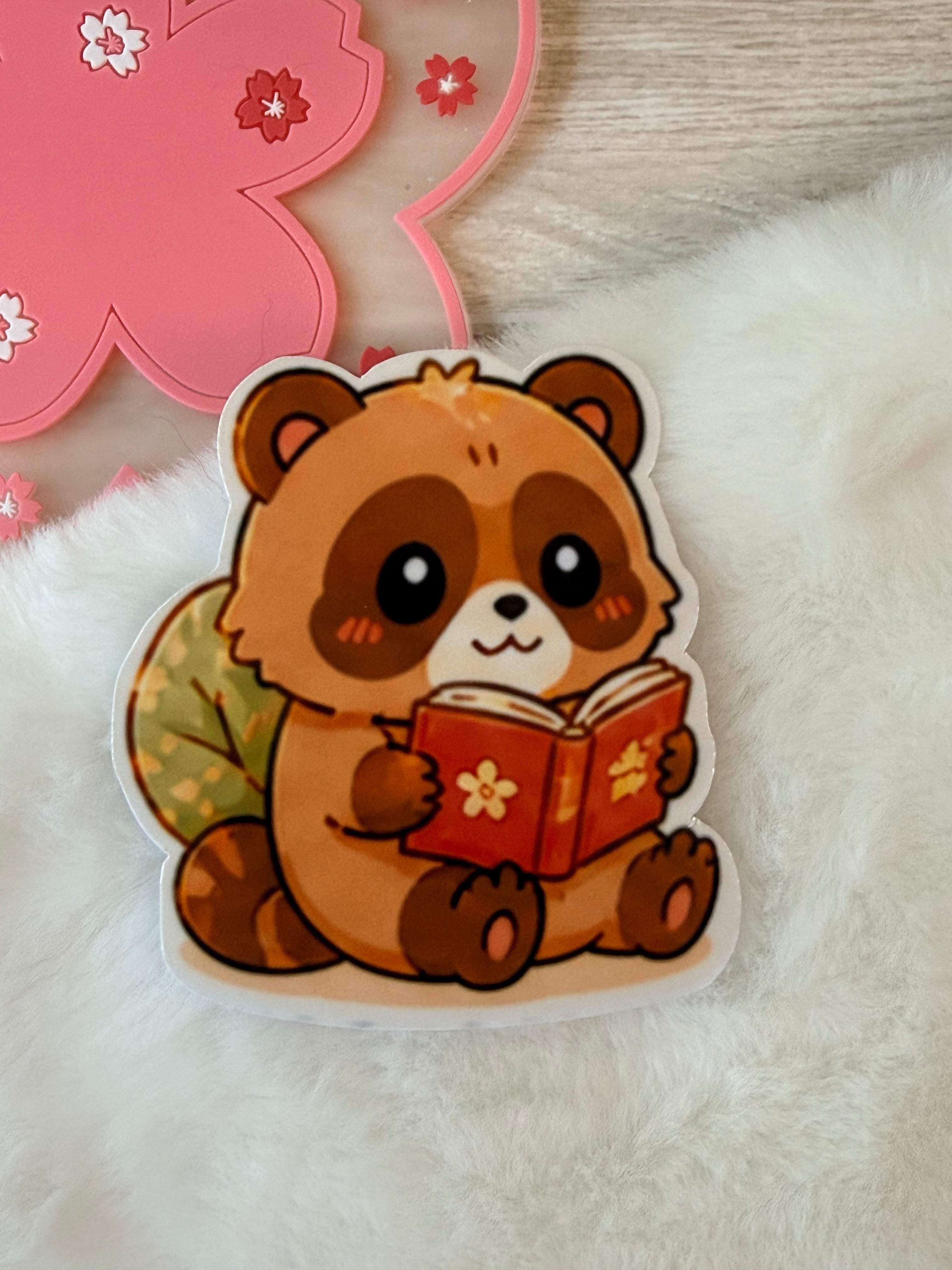 Sticker of Tanuki holding a book on a fluffy white surface