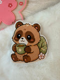 Sticker of a Tanuki holding a mug on a fluffy white surface